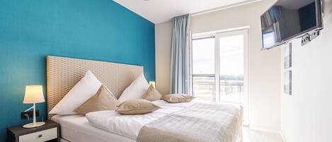 A bedroom with a bed, nightstand, lamp, and a TV mounted on the wall.