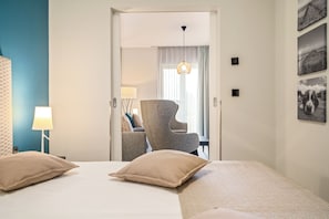 Une chambre d’hôtel avec un lit, deux oreillers, une chaise, une lampe et un mur décoré de tableaux.