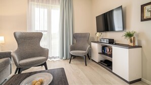 A modern living room with two grey armchairs, a flat-screen TV, a small white cabinet, and a dining table with a plate of nuts. - Ostseestuv – 5-Star Vacation Rental Between the Baltic Sea and the Bodden (Wustrow)