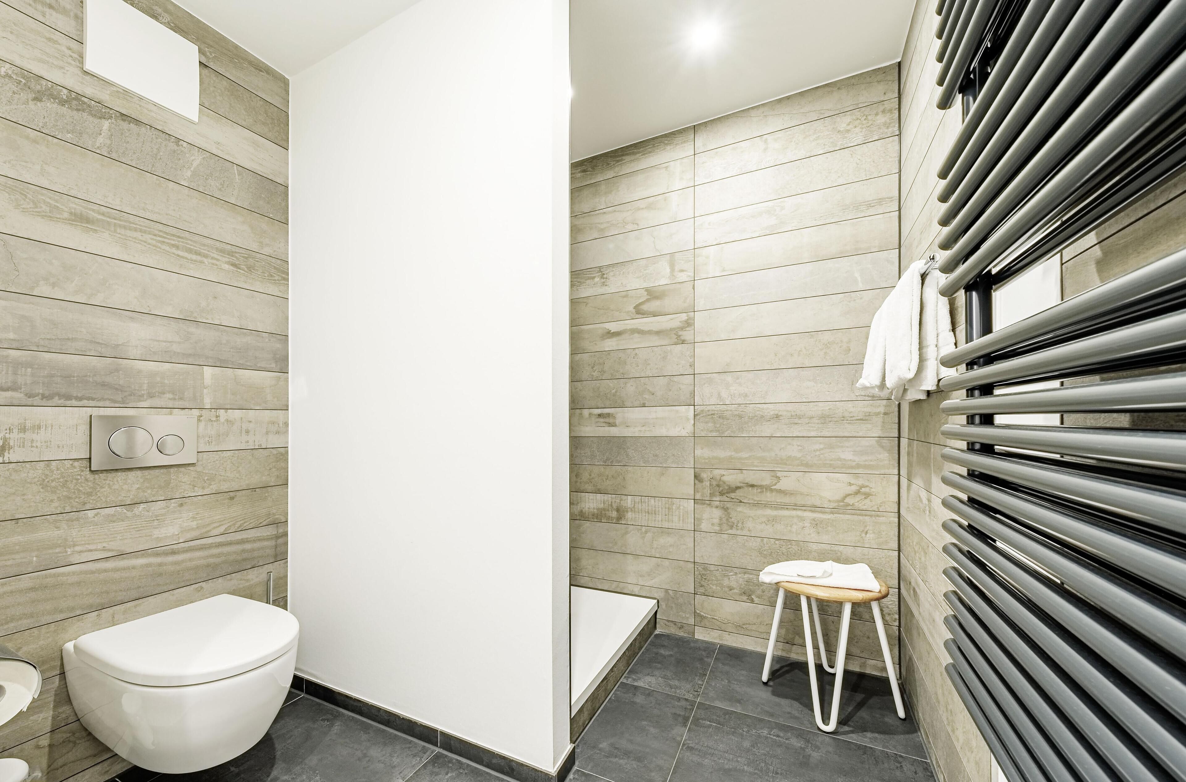 A modern bathroom with a toilet, a small stool, a towel rack, and a shower area.