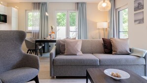Una sala moderna con un sofá gris, una mesa de centro de madera y un sillón gris. Se ve una mesa de comedor con sillas al fondo.