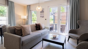 Una sala de estar moderna con un sofá gris, una mesa de centro y una silla. Hay una lámpara, una ventana con cortinas y vistas al exterior.