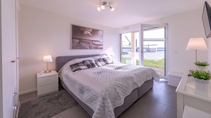 A bedroom with a bed, nightstands, a lamp, a painting, and a view through a glass door.