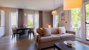 A modern living room with a sofa, dining table, and chairs. There is a large window with curtains, a hanging light fixture, and a plant on the windowsill. - 5 star vacation apartment "Seesinn" in Wustrow on the Baltic Sea (Wustrow)