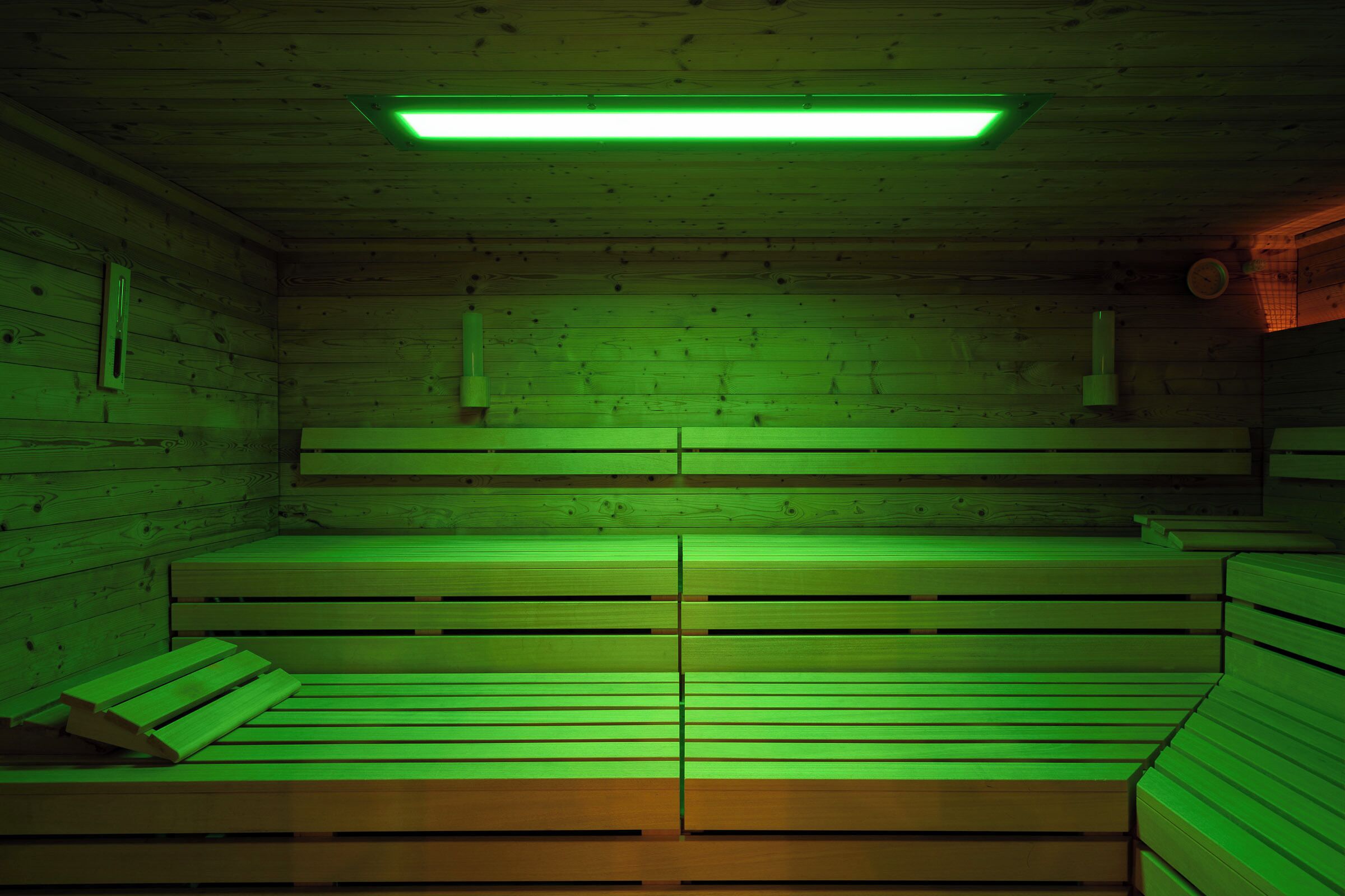 A sauna room with wooden benches and a green-lit ceiling.