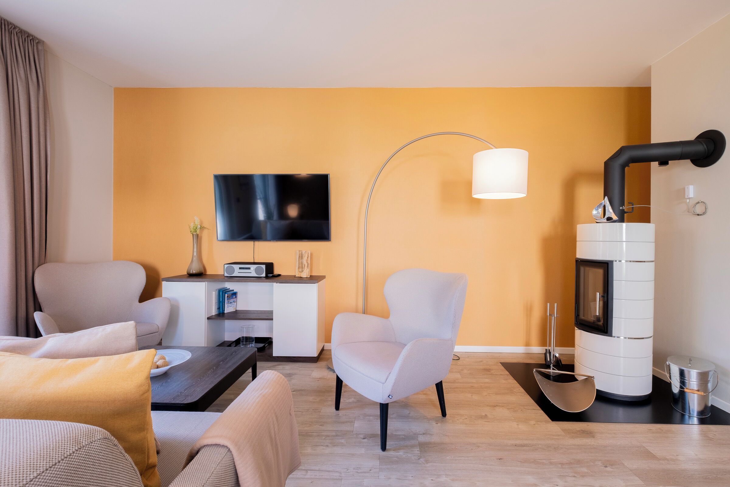 A modern living room with a sofa, armchairs, a coffee table, a flat-screen TV, a lamp, and a fireplace.