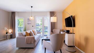 Un salon moderne avec un canapé, un fauteuil et un téléviseur à écran plat fixé au mur.