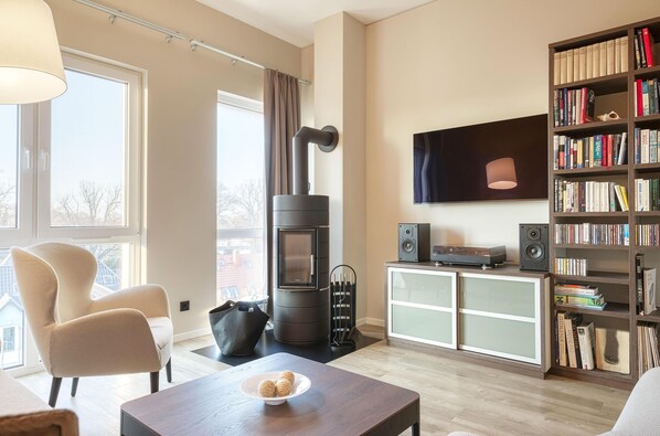 Ein modernes Wohnzimmer mit einer Couch, einem Tisch mit Keksen, einem Kamin, einem Bücherregal und einem an der Wand montierten Fernseher.