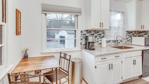 A kitchen with white cabinets, a wooden table, and a window with blinds. - 7 Mi to Downtown Minneapolis: Home w/ Fire Pit! (Richfield)