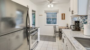 A modern kitchen with stainless steel appliances, a dining area with a wooden table and chairs, and a window with a view of trees. - 7 Mi to Downtown Minneapolis: Home w/ Fire Pit! (Richfield)