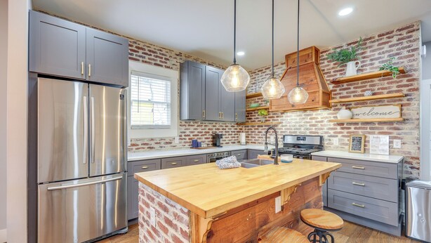 A kitchen with a stainless steel refrigerator, wooden island, bar stools, and a brick wall. - ~ 2 Mi to Dtwn San Antonio: Comfy Home w/ Yard! (San Antonio)