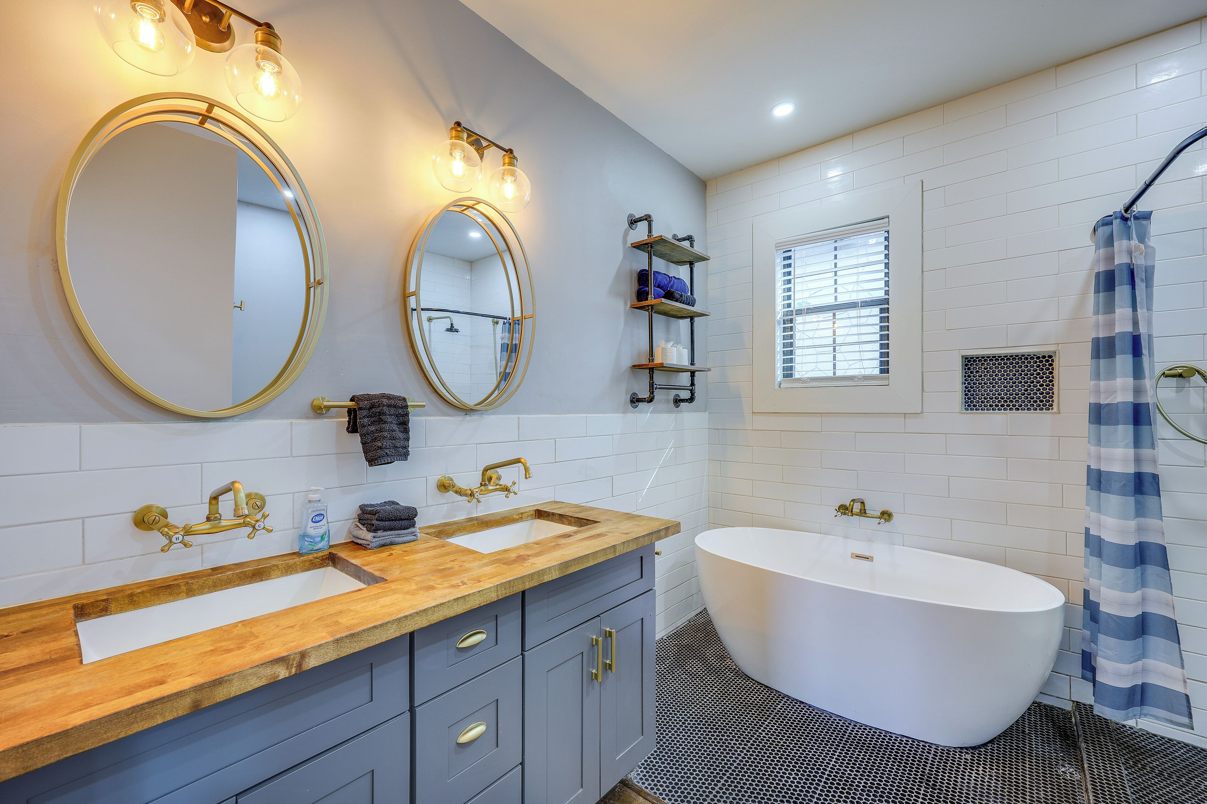 A bathroom with a wooden vanity, a freestanding bathtub, and a large mirror with lights.