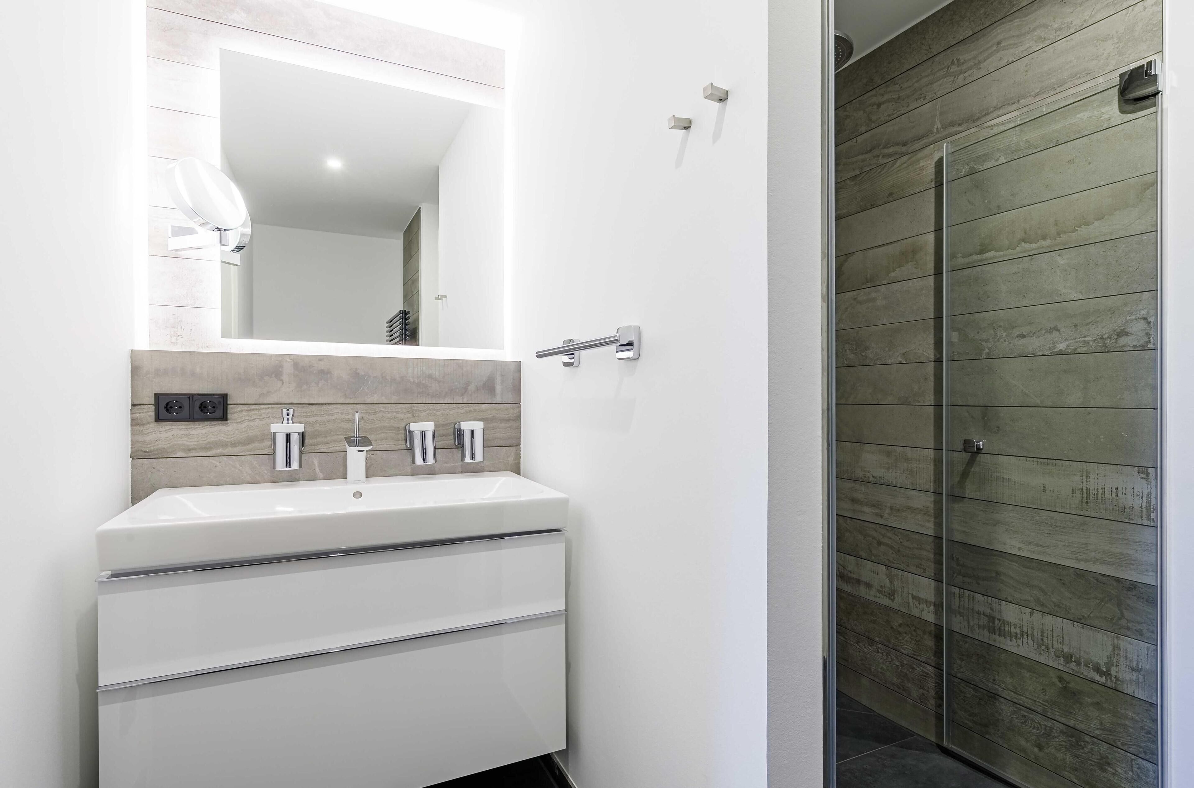 Un baño moderno con un lavamanos blanco, un espejo y un panel de pared de madera.