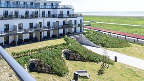 A modern multi-story building with balconies, a landscaped garden, and a view of the sea.