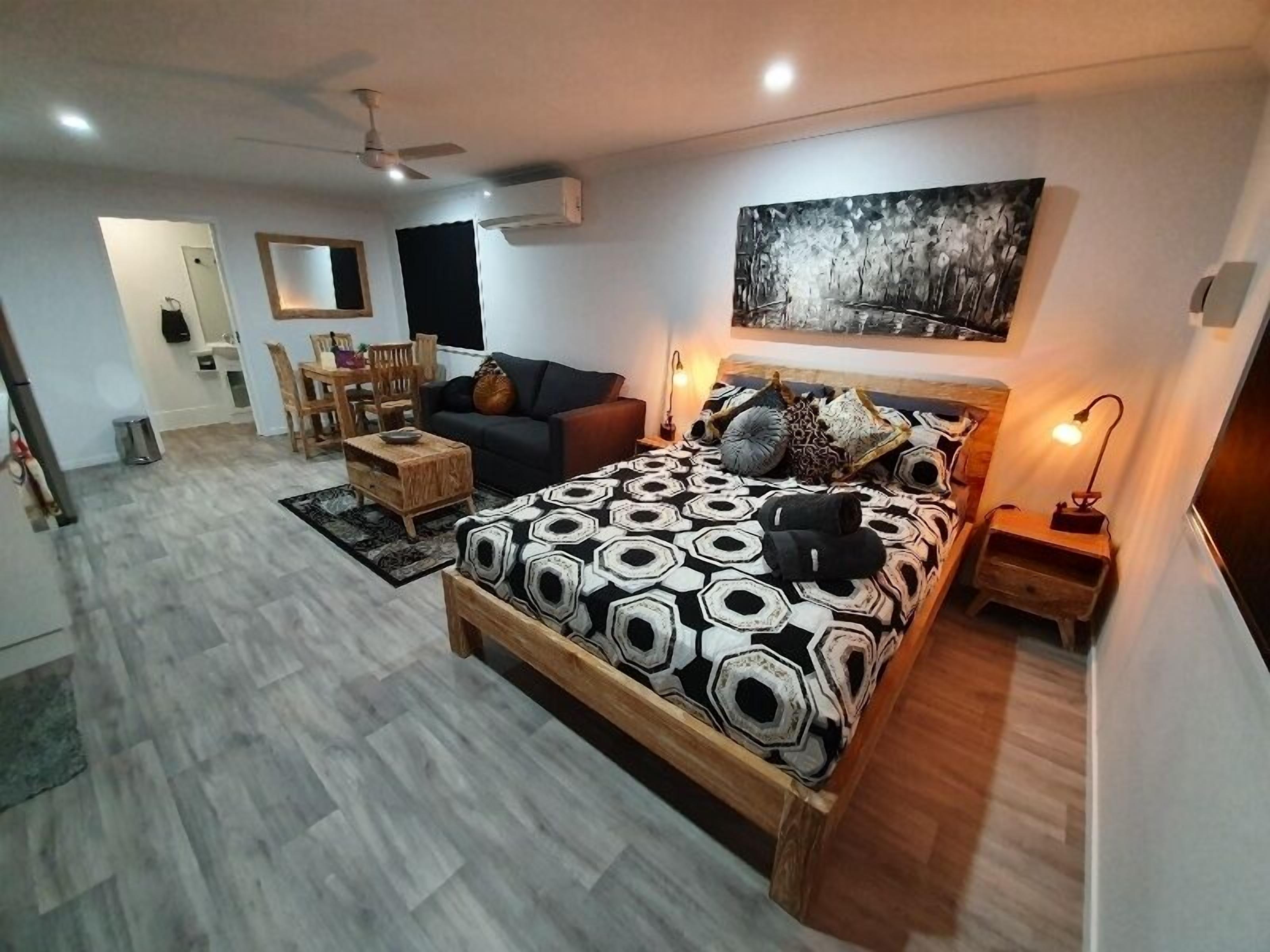A modern bedroom with a large bed, a sofa, a dining area, and a ceiling fan.