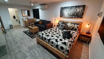 A modern bedroom with a large bed, a sofa, a dining area, and a ceiling fan.