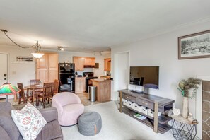 A modern living room with a sofa, ottoman, and a dining area with chairs and a table. A kitchen with wooden cabinets and appliances is visible in the background. - Skiing & Hiking: Mtn-view Condo in Durango! (Durango)