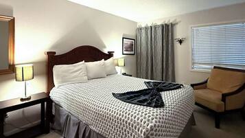 Habitación de hotel con cama, una silla, lámpara, un cuadro en la pared y una ventana con persianas.