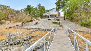 A pathway leading to a house with a balcony, surrounded by trees and a rocky landscape. - 'the Waterfront Gem' w/ Dock in Osage Beach! (Osage Beach)