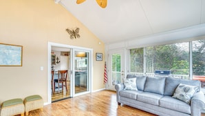 A spacious living room with a gray sofa, wooden flooring, and a large window offering a view of the outdoors. - 'the Waterfront Gem' w/ Dock in Osage Beach! (Osage Beach)
