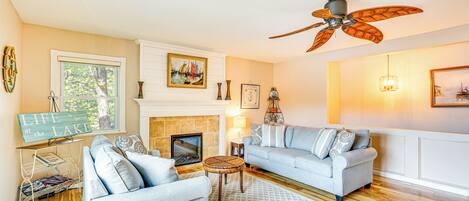 A living room with a fireplace, two sofas, a ceiling fan, and a bookshelf.