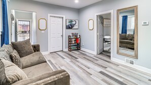 Un salon avec un canapé d’angle beige, un plancher en bois et une porte donnant sur un couloir.