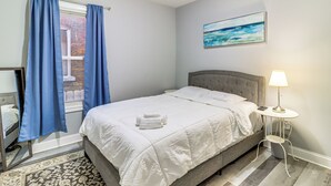 Une chambre à coucher avec un lit, une table de chevet avec une lampe, une fenêtre avec des rideaux et un tableau accroché au mur.