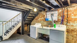 Une buanderie équipée de deux machines à laver, d’un escalier et d’un mur en briques.