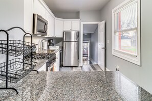 A kitchen with white cabinets, a stainless steel refrigerator, a microwave, and a black metal rack. - Downtown Detroit Townhome Near North End! (Detroit)