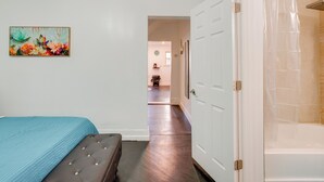 A bedroom with a bed, a bench, a door leading to a bathroom, and a hallway. - 1 Mi to Train Station: Quiet Apartment in Newark (Newark)
