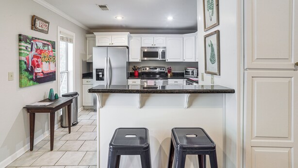 A kitchen with white cabinets, a granite countertop, stainless steel appliances, and two stools. - Private Deck, 1 Block From The Square (Oxford)