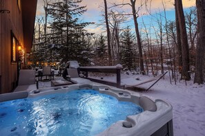 Un bain à remous installé à l’extérieur, dans un décor enneigé, avec une terrasse en bois et des chaises.