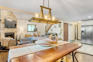 Un vaste salon avec une table à manger en bois, une cheminée et, au fond, une cuisine moderne.