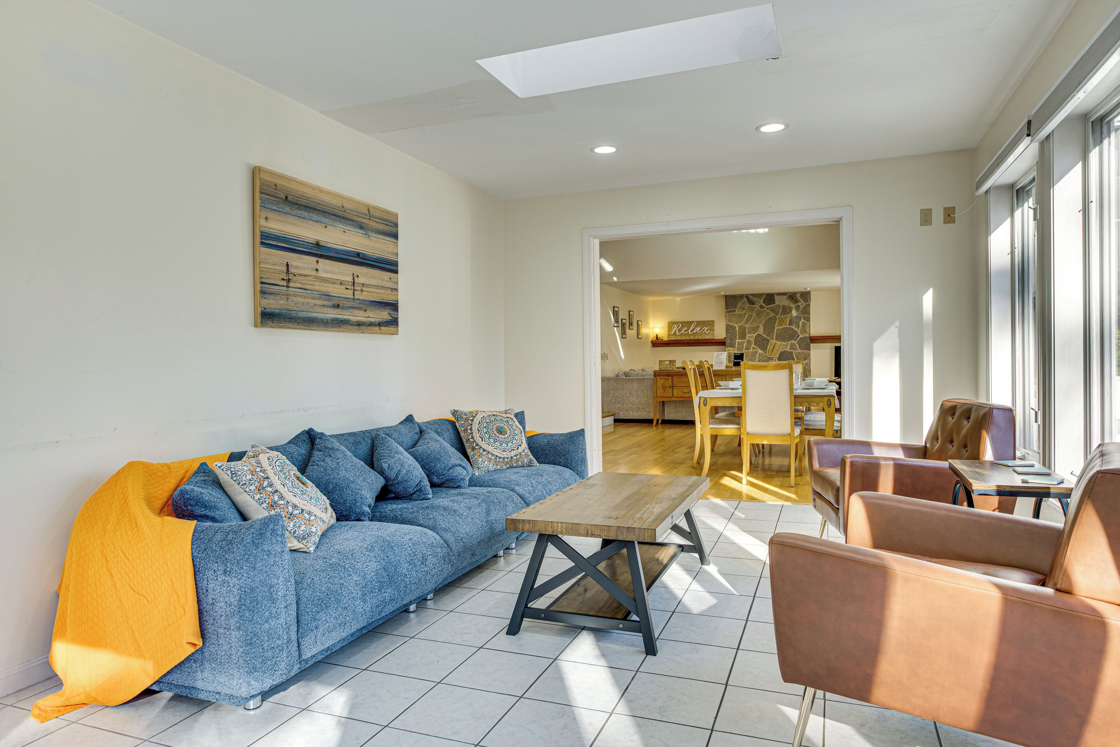 Un salon moderne avec un canapé, une table basse et des fauteuils. On aperçoit à l’arrière-plan un coin repas avec une table et des chaises.