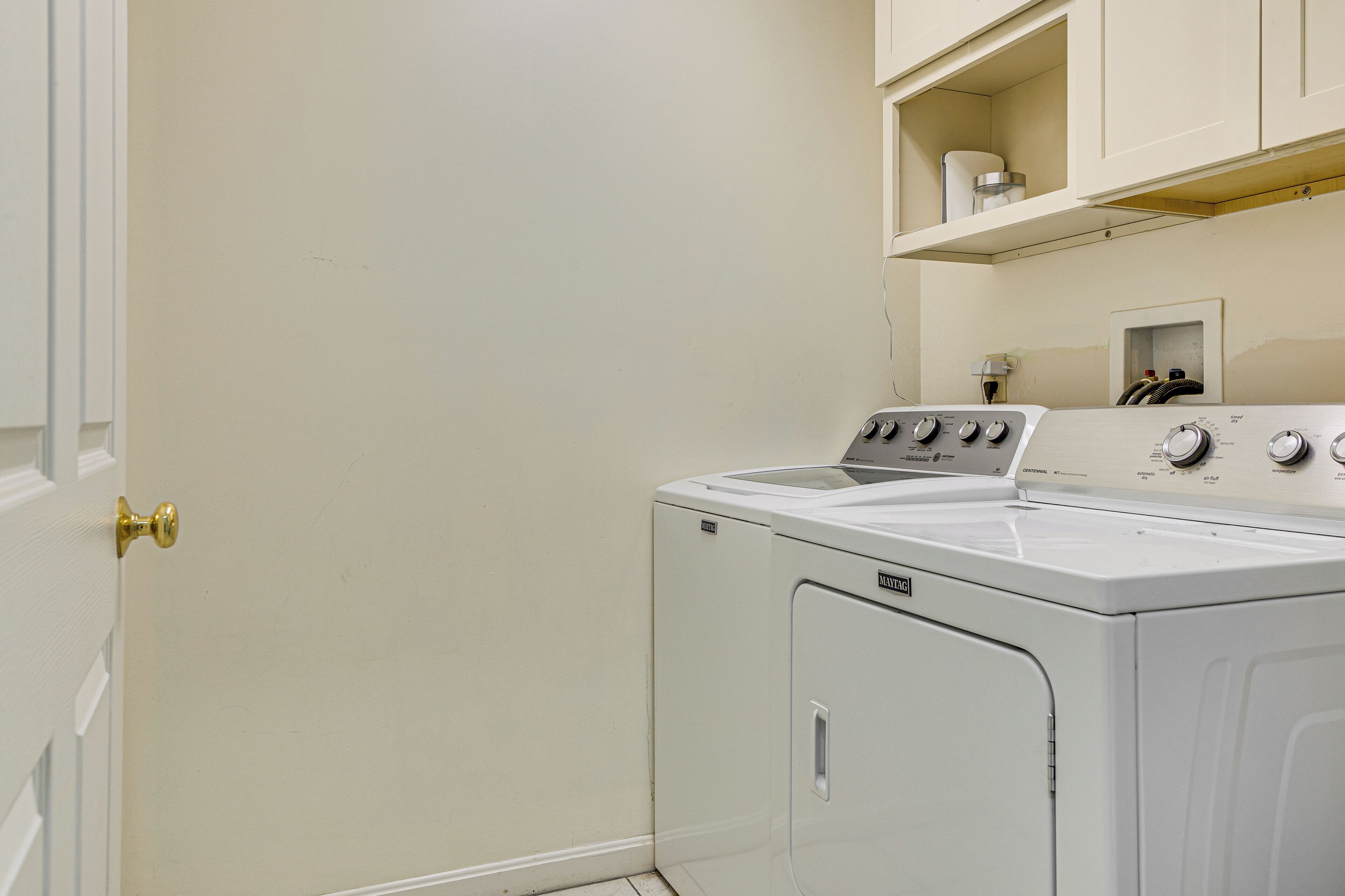 A compact laundry room with a washing machine and dryer, a white door, and a shelf above the dryer.