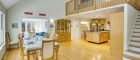 A spacious open-plan living area with a dining table and chairs, a kitchen with wooden cabinets, and a wooden staircase leading to an upper level.