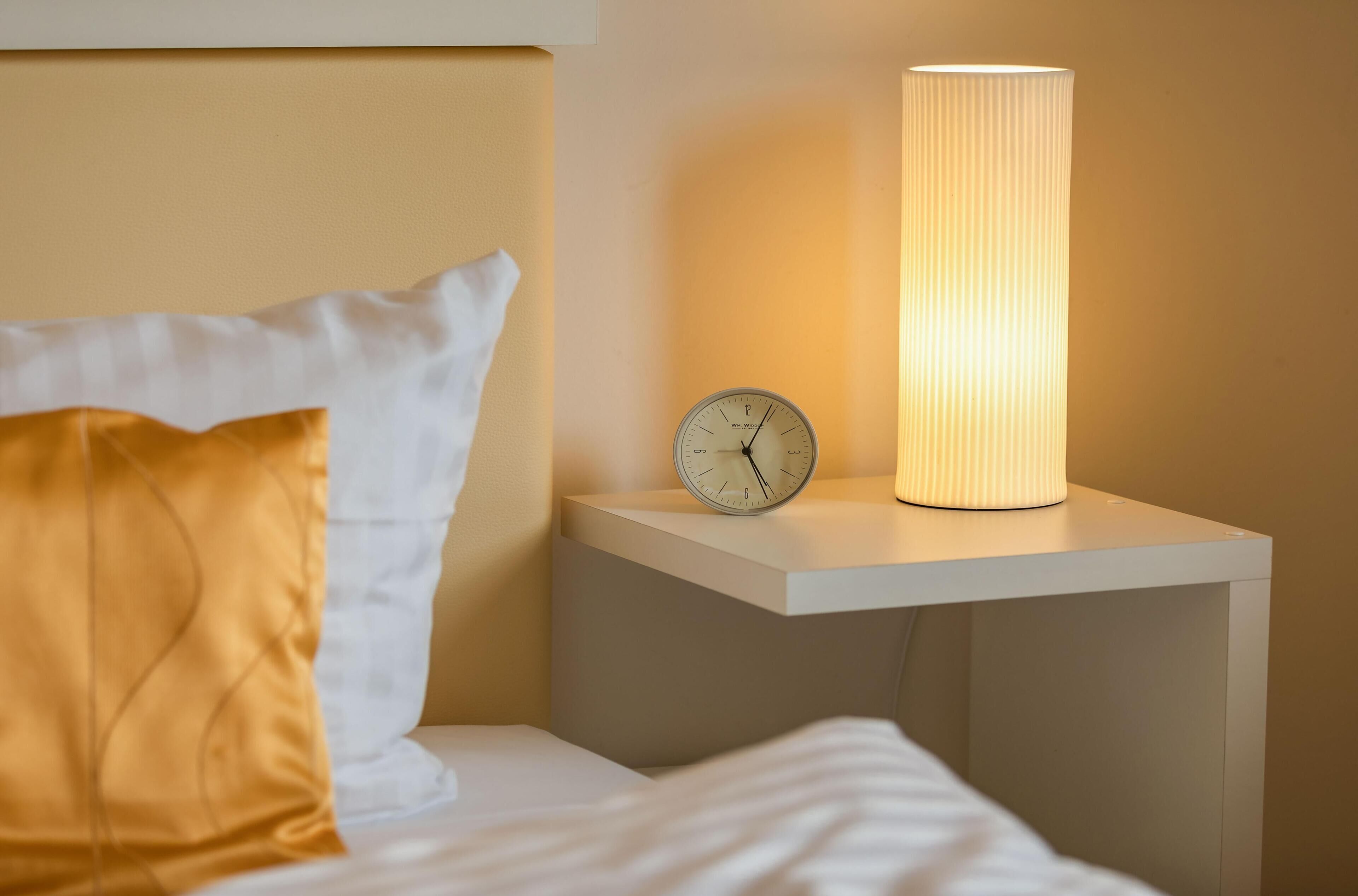 Une table de chevet avec une horloge et une lampe cylindrique.