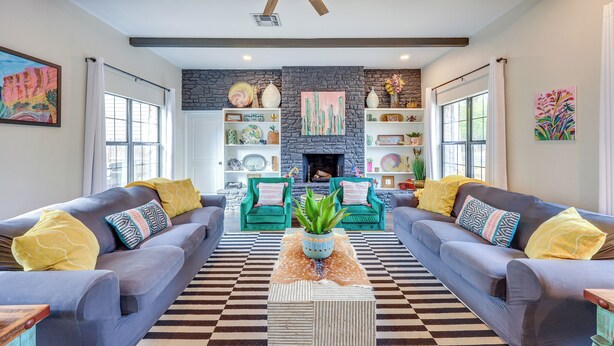 A living room with two grey sofas, a black and white checkered rug, and a stone fireplace. - < 1 Mi to Dtwn: Home w/ Fenced Yard in Boerne! (Boerne)