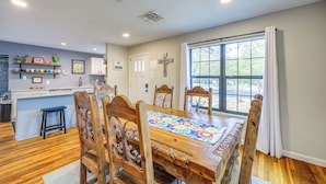 A dining area with a wooden table, chairs, and a window with curtains. - < 1 Mi to Dtwn: Home w/ Fenced Yard in Boerne! (Boerne)