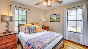 A bedroom with a bed, wooden nightstands, a ceiling fan, and large windows with curtains. - < 1 Mi to Dtwn: Home w/ Fenced Yard in Boerne! (Boerne)