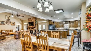 A spacious living area with a dining table, wooden chairs, and a fireplace. There is a kitchen with wooden cabinets and a large island. - 4 Mi to Dtwn: Home w/ Pool in Stephenville! (Stephenville)