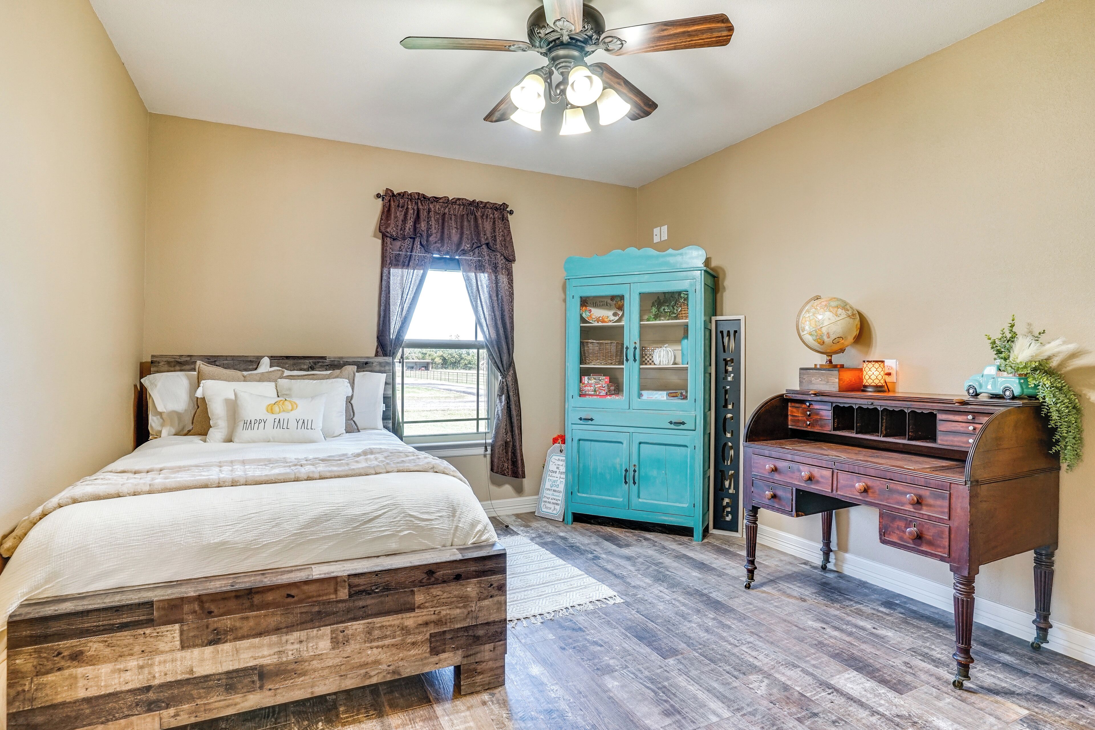 A bedroom with a wooden bed, a teal cabinet, and a desk with a globe and a toy car.