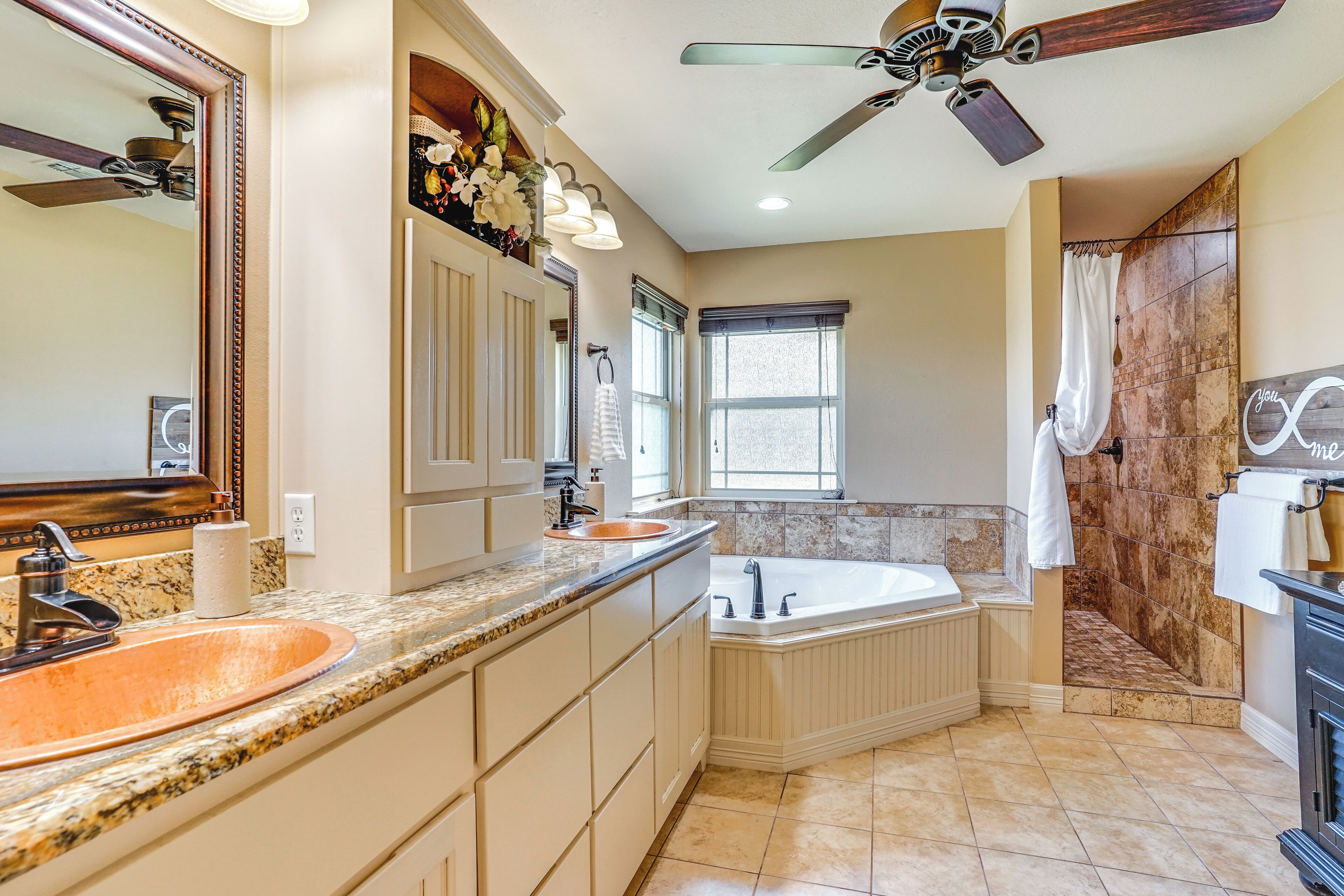 A bathroom with a double sink, a bathtub, a shower, and a ceiling fan.