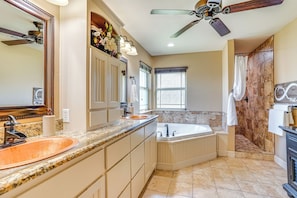 A bathroom with a double sink, a bathtub, a shower, and a ceiling fan.