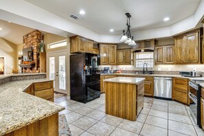 A spacious kitchen with granite countertops, wooden cabinets, a central island, and a built-in stove.