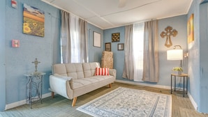 Uma sala de estar com sofá bege, tapete estampado e pequena mesa lateral com abajur.