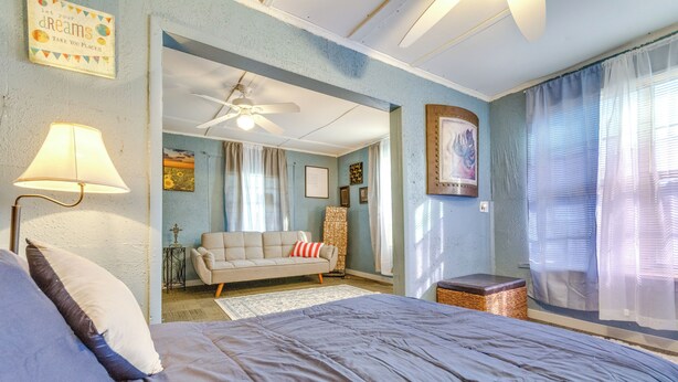 Quarto com cama grande, ventilador de teto, sofá e uma mesinha.