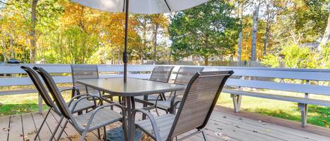 An outdoor patio with a round table and chairs, surrounded by a wooden deck and a white fence.