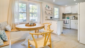 A kitchen with white cabinets, a microwave, and a stove. There is a dining table with chairs and a window with curtains. - Bike to Private Beach: Cape Cod Escape w/ Sunroom (East Falmouth)