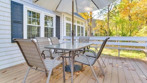 An outdoor patio with a table and chairs, a large umbrella, and a view of a house with shutters. - Bike to Private Beach: Cape Cod Escape w/ Sunroom (East Falmouth)